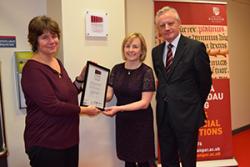 Sarah Horton of the Museums Archives and Libraries Division of the Welsh Government presents the accreditation certificate to Elen Wyn Simpson in the presence of University Vice-Chancellor Prof John G Hughes.